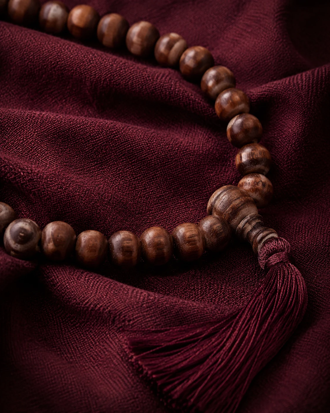 Illustrative close-up of brown mala beads and a burgundy tassel on dark red fabric